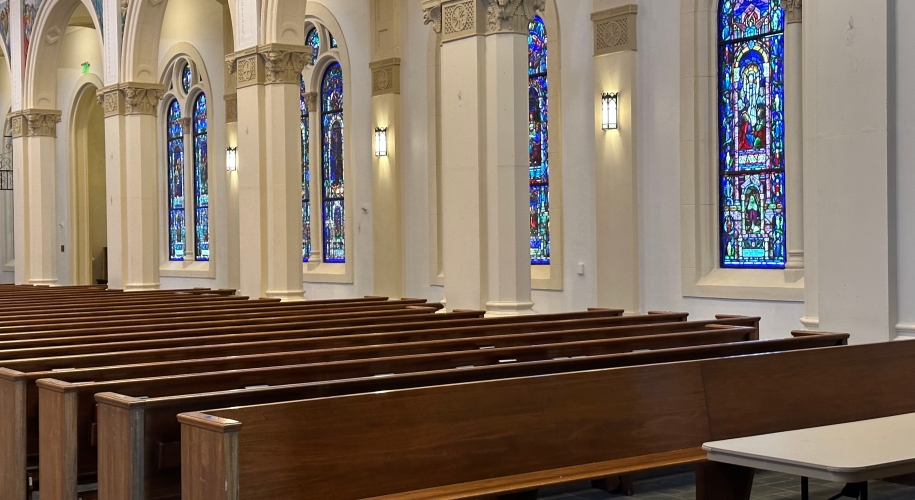 A row of wooden pews with stained glass and columns visible in the background.